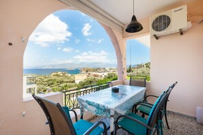Ein Balkon mit Tisch und Stühlen, einer Klimaanlage und Blick auf Meer und Landschaft.