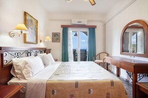 Ein Hotelzimmer mit Bett, Nachttischlampen, Schreibtisch, Stuhl, Spiegel und Blick ins Freie.