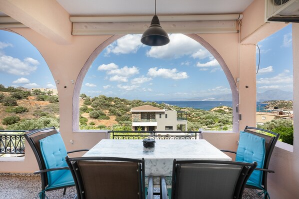 Ein Balkon mit Tisch und Stühlen mit Blick auf eine Küstenlandschaft, die Gebäude und Vegetation zeigt.