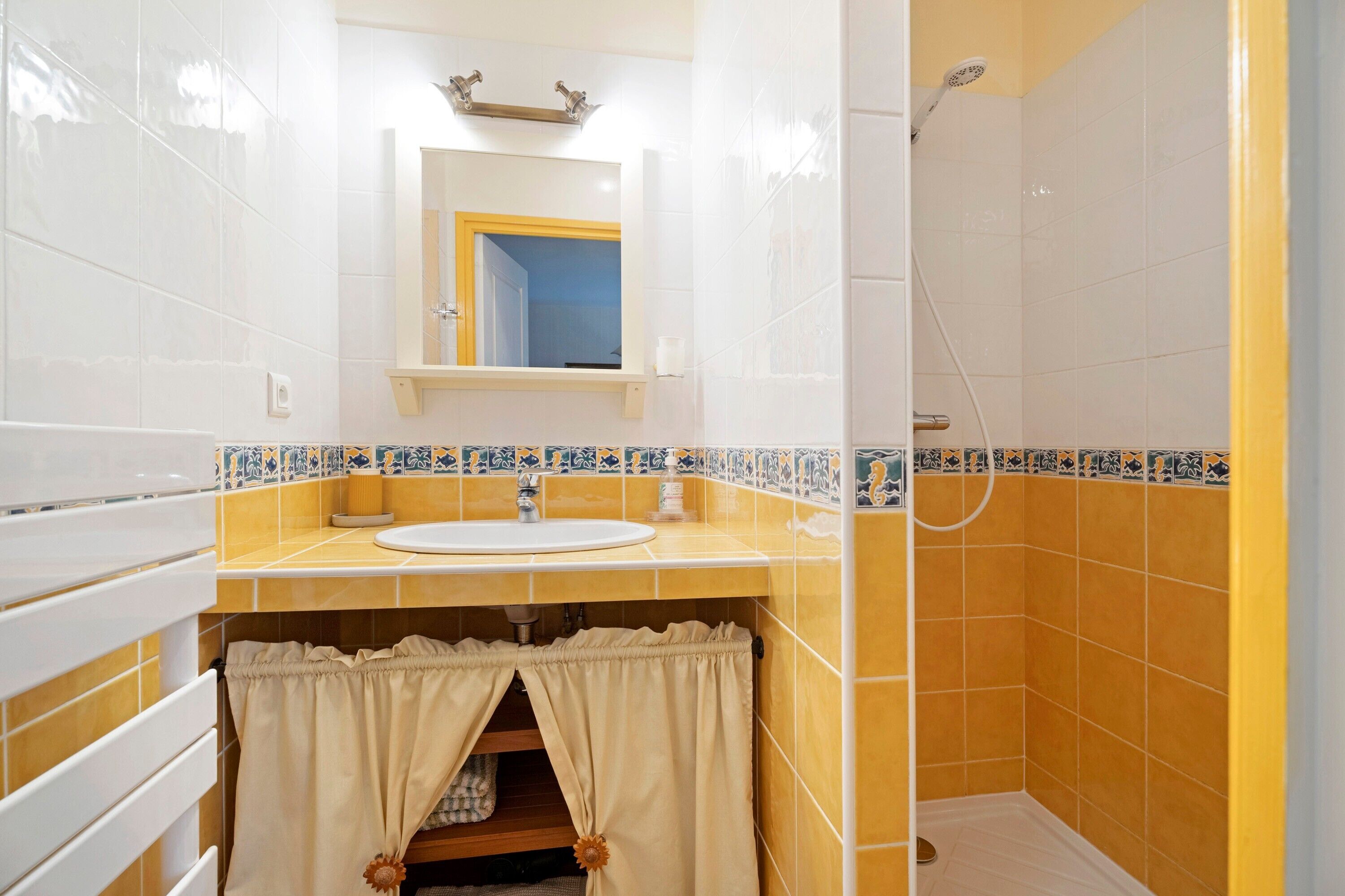 Ein Badezimmer mit Waschbecken, Spiegel, Dusche und gefliesten Wänden.