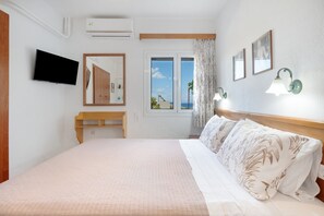 Een hotelkamer met een bed, een televisie, een bureau, een raam met uitzicht en wandlampen.