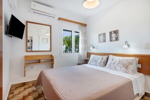 Un dormitori amb un llit, televisió, finestra amb cortines, mirall i llums penjades a la paret.