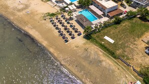 An aerial view of a coastal hotel with a swimming pool, beachside lounge chairs, and a beach.
