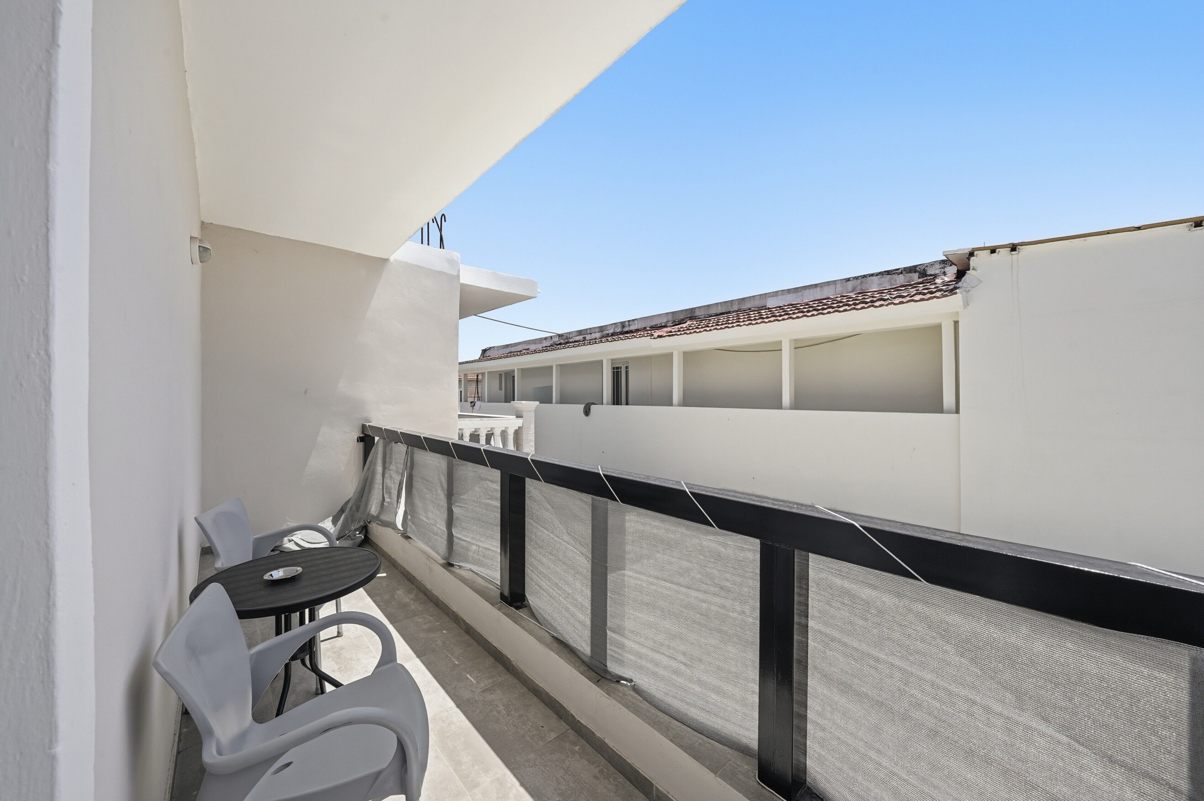 Un balcon avec une table et des chaises, un mur blanc et un bâtiment en arrière-plan.
