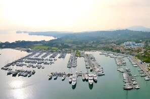 Ilmakuva venesatamasta, jossa on useita laivoja laiturissa. Satamaa ympäröi kumpuileva maisema ja rakennuksia.