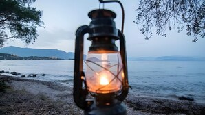 Una lanterna su una spiaggia con vista sul mare e sulle montagne sullo sfondo.