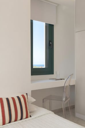 Ein modernes Zimmer mit einem Bett, einem Schreibtisch mit Stuhl, einem Fenster mit Blick und einem kleinen Tisch mit einem Glas.
