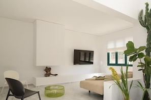 Ein modernes Wohnzimmer mit einem weißen Sofa, einem schwarzen Sessel, einem grünen Glastisch, einem wandmontierten Fernseher und einer Kakteenpflanze.