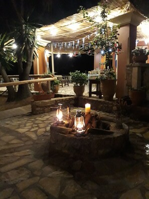 An outdoor patio area with stone flooring, a fire pit with candles, potted plants, and a covered seating area. - Gouvia Studio 5 – Stylish with Pool Access (Kontokali)