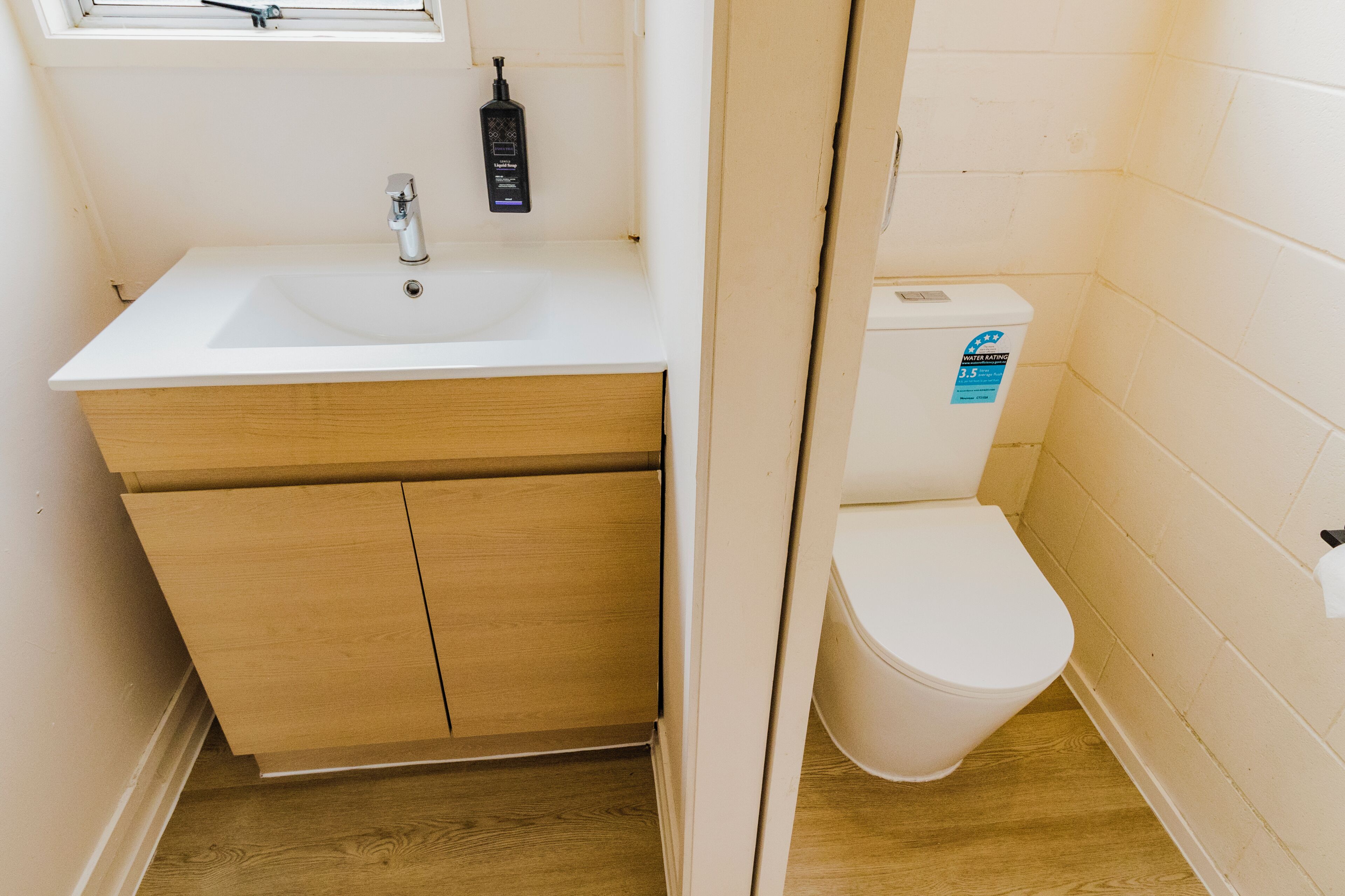 A small bathroom with a white sink, wooden vanity, and a white toilet.