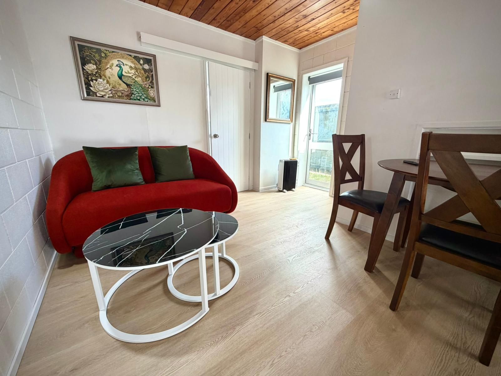 Una habitación con un sofá rojo, una mesa de vidrio, una silla de madera y un cuadro en la pared.