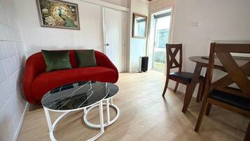 Una habitación con un sofá rojo, una mesa de vidrio, una silla de madera y un cuadro en la pared.