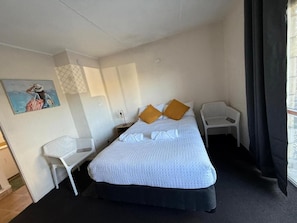 Ein Hotelzimmer mit Bett, Schreibtisch, Stuhl, einem Bild an der Wand und einem Fenster mit Vorhängen.