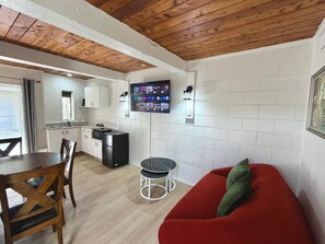 A compact living space with a dining area, kitchenette, and a red sofa with a green pillow. - Central Stay Hinemaru (Rotorua)