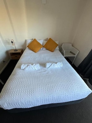 Ein Hotelzimmer mit Bett, zwei Kissen, einem Nachttisch, einem Sessel und einer Lampe.