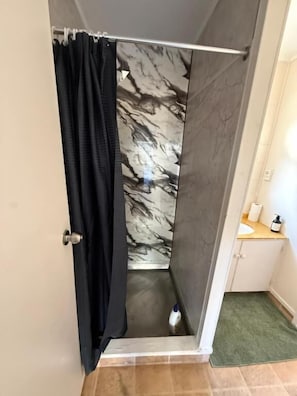 Ein Badezimmer mit einer Duschwand aus Marmor, einem schwarzen Duschvorhang, einem weißen Waschbecken und einer grünen Fußmatte.