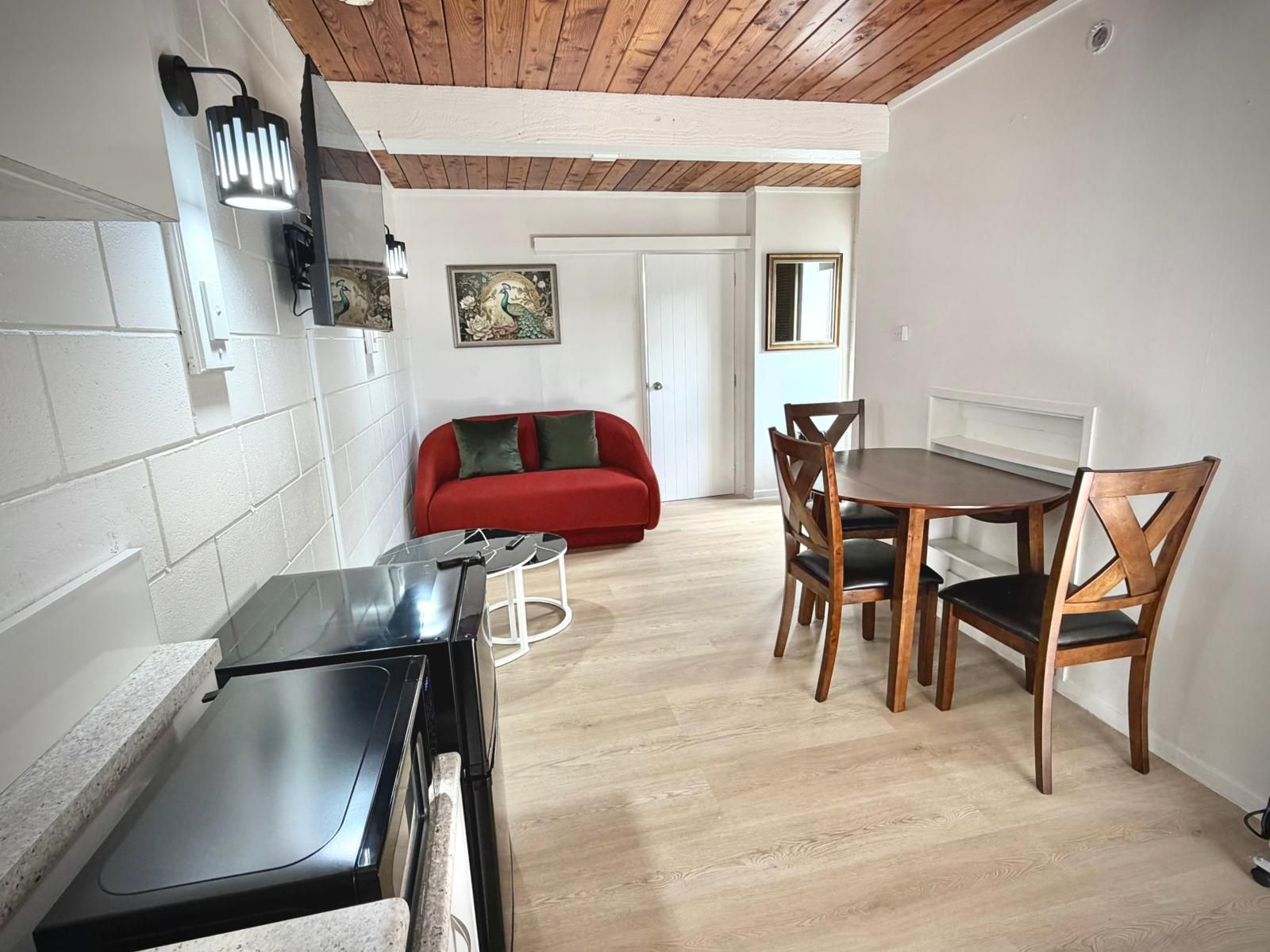 A compact living space with a dining area, a red sofa, and a wooden dining table with chairs.
