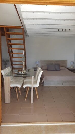 Une chambre à coucher comprenant un lit, des tables de chevet, un bureau avec des chaises, un ventilateur et une échelle en bois.