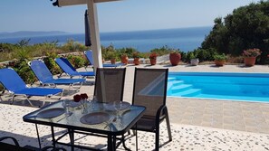 Un espace aménagé au bord de la piscine, avec une table pour deux, des chaises longues bleues et des plantes en pot.
