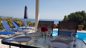 Une table dressée pour un repas, avec une piscine et des chaises longues en arrière-plan.