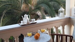 A balcony with a table set for breakfast, including a pitcher, cups, and glasses of orange juice, with a view of palm trees. - Family 2BR Apt Pool – Kitchenette 7 (Kontokali)