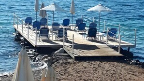 A pier with chairs and umbrellas, a sandy beach, and the sea. - Comfy Stay Gouvia – Kitchenette 4 (Kontokali)