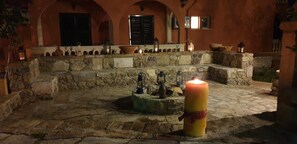 Un pati de pedra amb una espelma, fanals i una paret rústica.