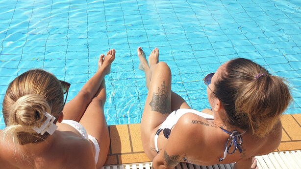 Two individuals relaxing by a pool with clear blue water. - Marina Balcony – Kitchenette 8 (Kontokali)