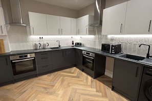 A modern kitchen with dark cabinetry, stainless steel appliances, and a herringbone wood floor. - Studio, West Kensington + Hammersmith (Greater London)