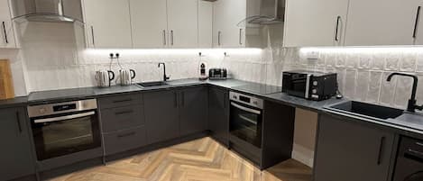A modern kitchen with dark cabinetry, stainless steel appliances, and a herringbone wood floor.