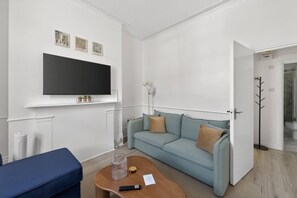 A modern living room with a sofa, a coffee table, a TV, and a coat rack. - Finsbury Park | Stylish 1BR | Near Tube | Wifi (Greater London)