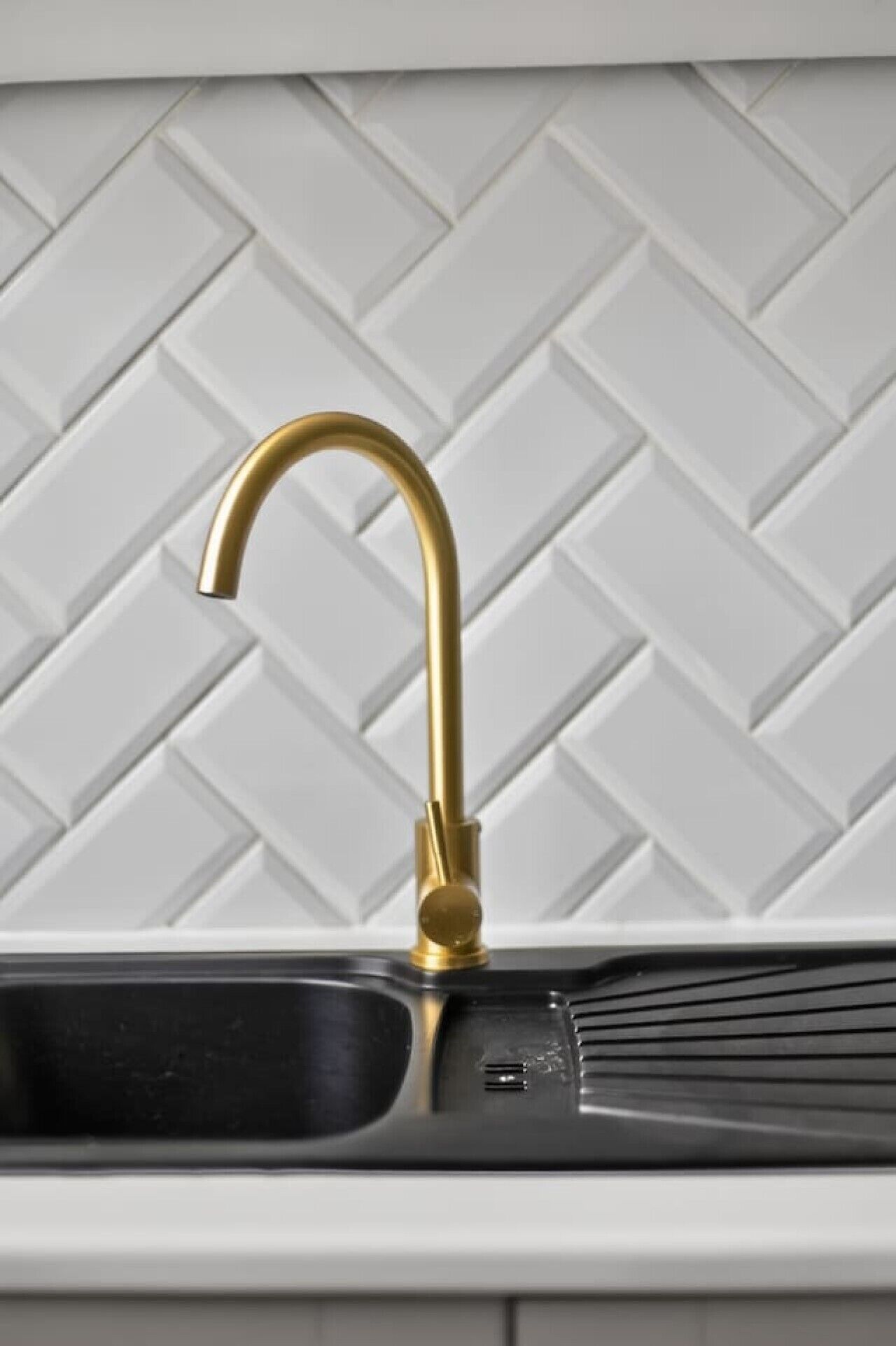 Eine Küche mit goldenem Wasserhahn, weißer Fischgrät-Spritzschutz und einem schwarzen Spülbecken.