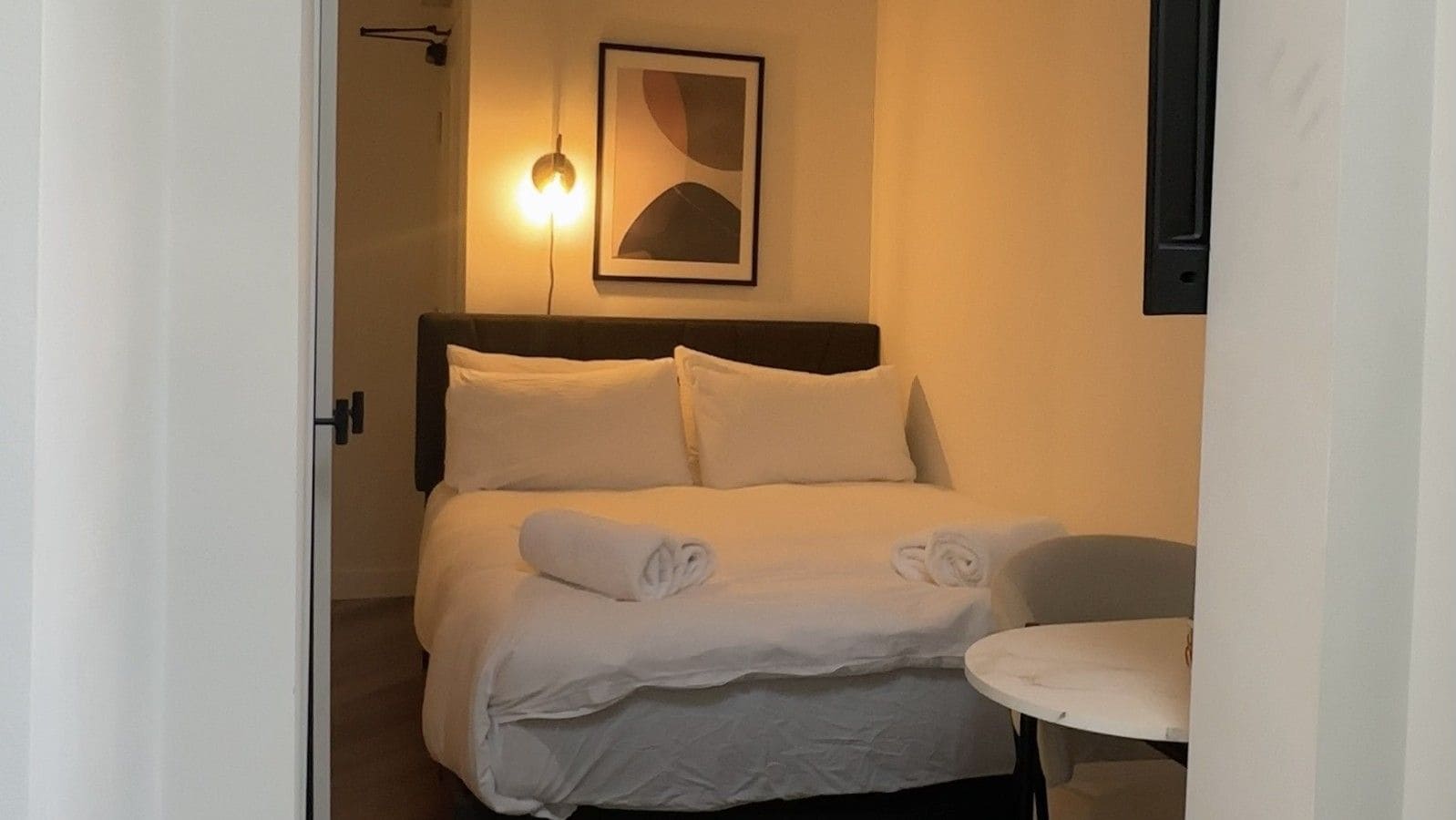 Une chambre d’hôtel avec un lit, une table ronde et un luminaire fixé au mur.