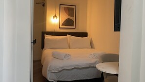 A hotel room with a bed, a round table, and a wall-mounted light fixture.