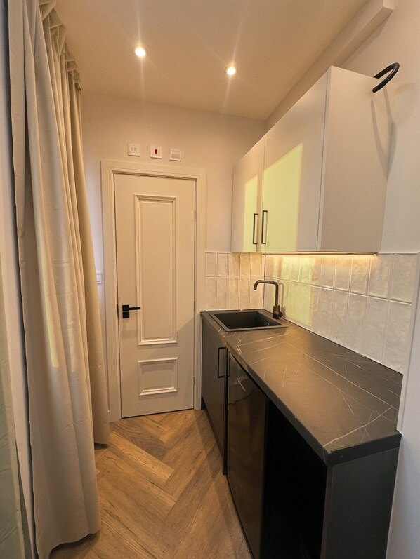 A compact kitchen with a single sink, white cabinets, and a herringbone-patterned floor.