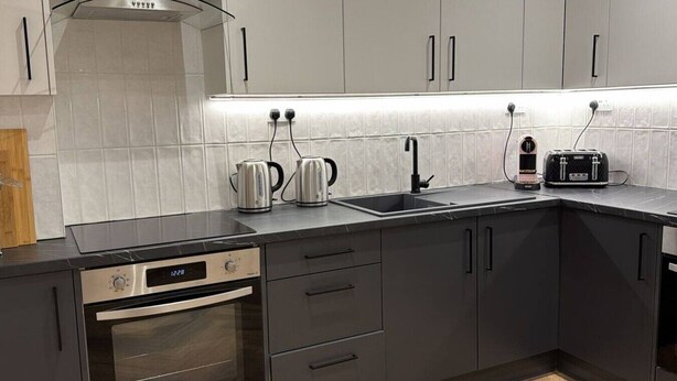 A modern kitchen with a built-in oven, a stovetop, a sink, and a kettle. - Modern Studio in Barons Court | Near Kensington & Hammersmith (Greater London)