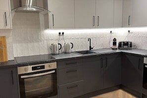 A modern kitchen with a built-in oven, a stovetop, a sink, and a kettle. - Modern Studio in Barons Court | Near Kensington & Hammersmith (Greater London)