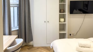 A modern bedroom with a bed, a TV mounted on the wall, a wardrobe, and a desk with a chair. - Modern Studio in Barons Court | Near Kensington & Hammersmith (Greater London)