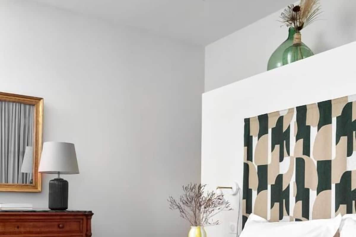 A bedroom with a bed, a nightstand, a lamp, a dresser, and a wall-mounted artwork.