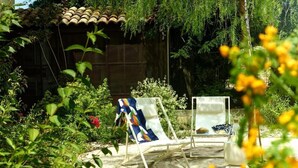 A garden with two lounge chairs, a tiled roof structure, and lush greenery. - Château de la Piscine - Appartements dans le Mas au coeur d'un grand parc arboré (Montpellier)