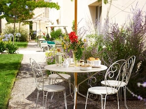 A round table with four chairs, a vase with flowers, and a spread of food and drinks. - Château de la Piscine - Appartements dans le Mas au coeur d'un grand parc arboré (Montpellier)