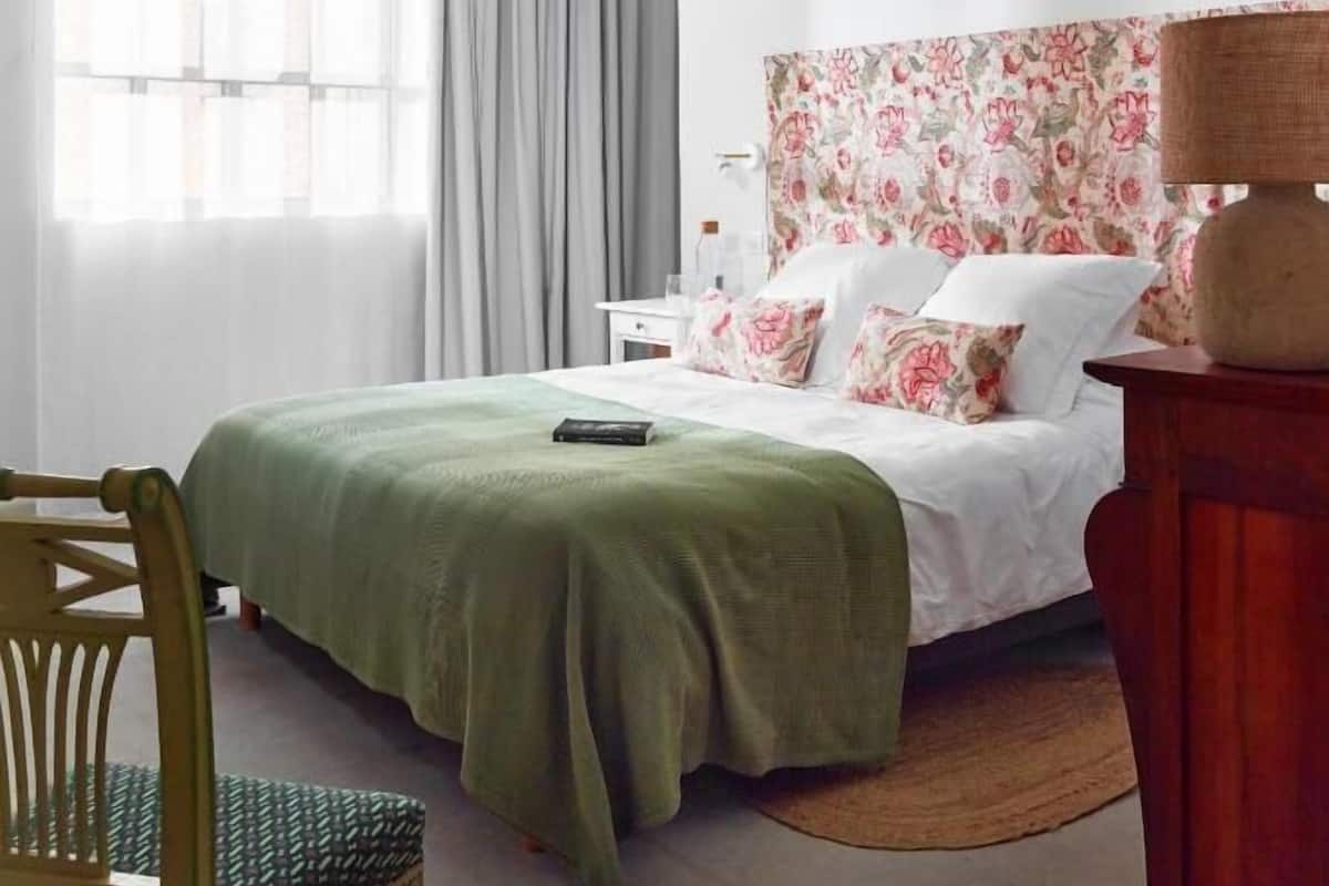 A bedroom with a bed, a chair, a nightstand, a lamp, and a window with curtains.