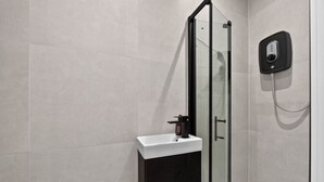 A modern bathroom with a glass shower enclosure, a sink with a faucet, and a wall-mounted control panel. - Studio, West Kensington + Hammersmith (Greater London)