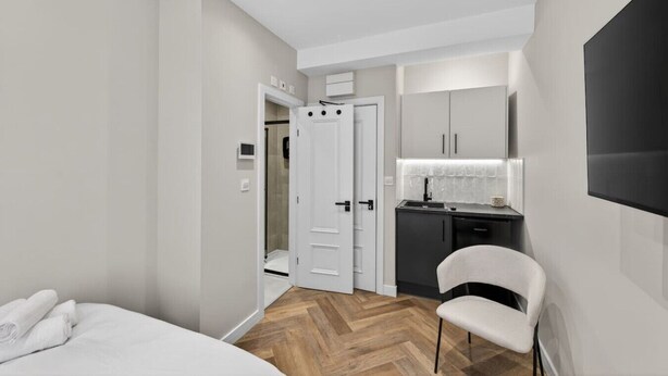 A modern hotel room with a bed, a chair, a kitchenette, and a shower area. - Studio, West Kensington + Hammersmith (Greater London)