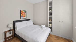 Een slaapkamer met een bed, nachtkastje, bedlamp, kledingkast en een lijst aan de muur.