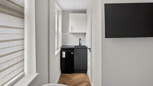 Een smalle gang die leidt naar een keuken met een zwarte koelkast, witte kasten en een zwarte televisie aan de muur.