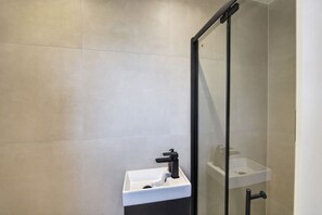 Un baño moderno con cabina de ducha de vidrio, un lavabo blanco y un grifo negro.