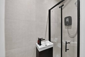 A modern bathroom with a glass shower enclosure, a white sink with a faucet, and a handheld showerhead. - Studio, West Kensington + Hammersmith (Greater London)
