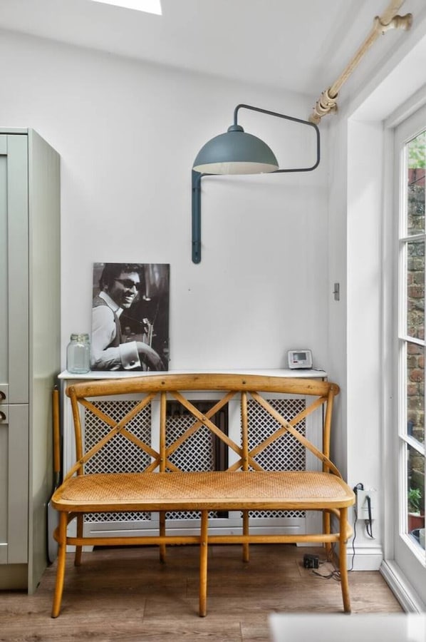 Una habitación de esquina con una silla de mimbre, una mesa, una lámpara de pared y un cartel.