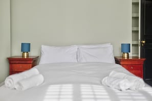 Una cama bien hecha con sábanas blancas, dos mesitas de noche con lámparas y un armario al fondo.